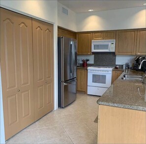 A modern kitchen with wooden cabinets, stainless steel appliances, and a granite countertop. - Oceanview Townhome w/ Pool Near Beaches & Shops (Kailua-Kona)