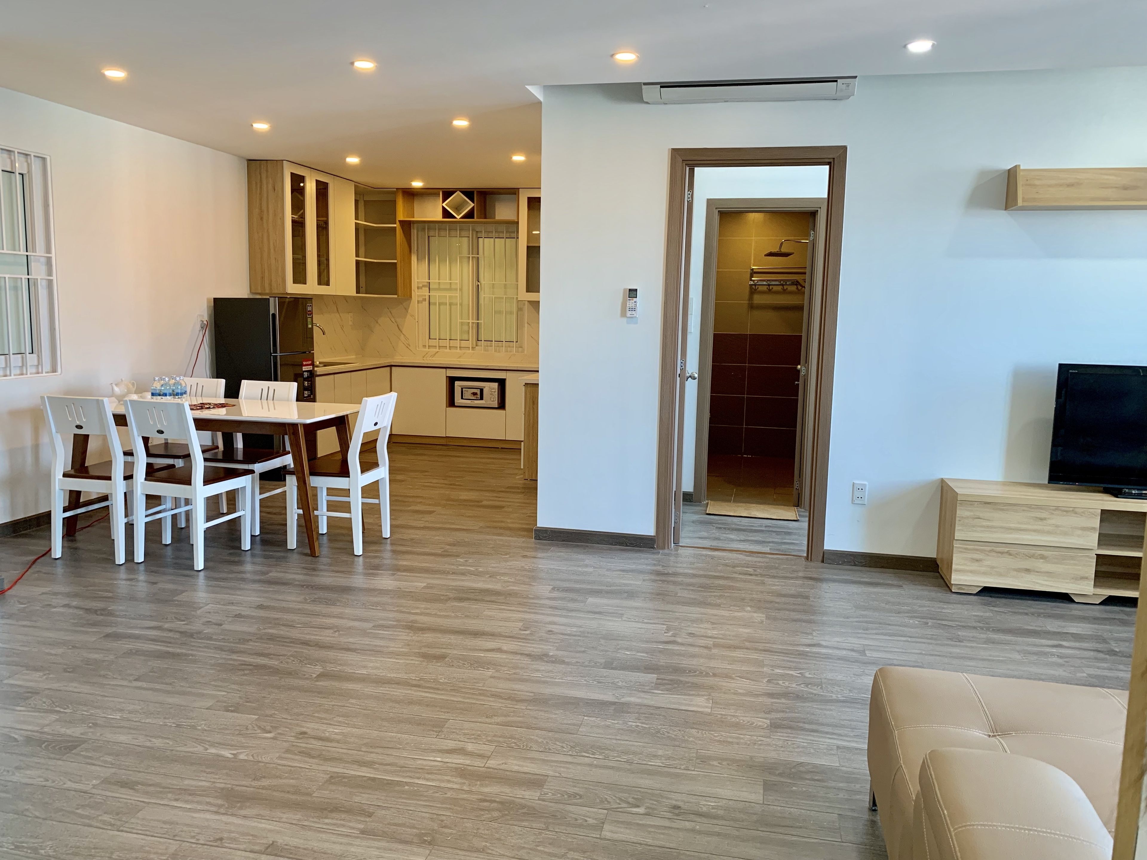 A modern living room with a dining area, wooden flooring, and a TV on a wooden stand.
