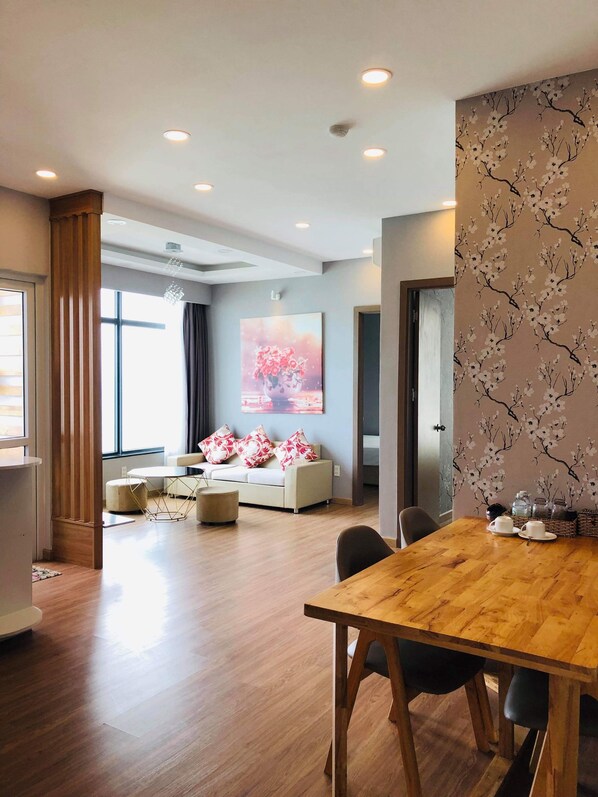 A modern living room with a wooden dining table, a sofa with decorative pillows, and a large floral painting on the wall.