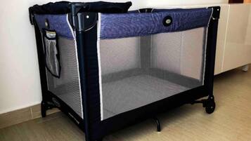 A portable crib with a mesh top and solid side panel, featuring a black frame and wheels for easy mobility.