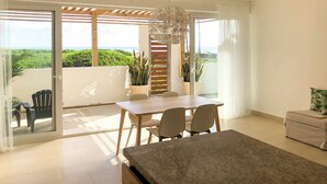 Un moderno comedor con una mesa, sillas, una lámpara en el techo y vista a follaje exuberante a través de una puerta corrediza de vidrio.