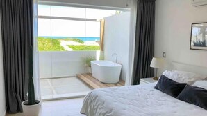 Un dormitorio moderno con una cama grande, una bañera y un balcón con vista al mar.
