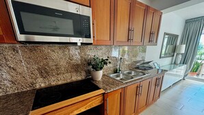 Cocina con gabinetes de madera, encimera de granito, microondas integrado, pileta de acero inoxidable y una planta en maceta.