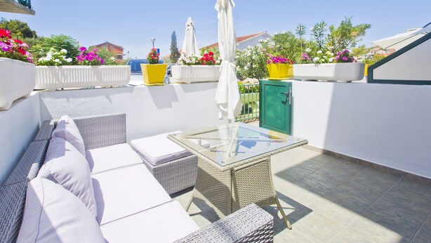 Terraza en la azotea con mobiliario de mimbre, una mesa de vidrio y plantas en macetas.