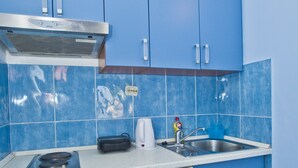 Cocina compacta con armarios azules, un refrigerador blanco, estufa, fregadero y hervidor.
