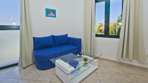 Una sala de estar con un sofá azul, una mesa de centro de vidrio y vistas a edificios a través de una ventana.