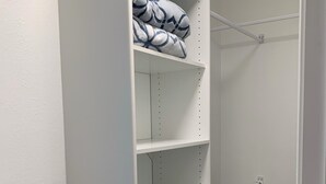 Un armario blanco con estantes, una barra para colgar ropa y una cesta de mimbre.