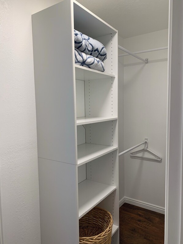 Un placard blanc avec des étagères, une tringle et un panier en osier.