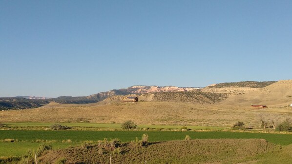A rural landscape with a large building on a hill, surrounded by fields and sparse vegetation.