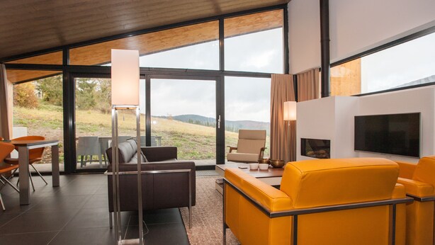 A modern living room with a large window, a sofa, a TV, and a dining area. - Villas Winterberg (Winterberg)
