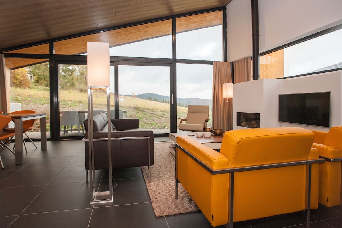 A modern living room with a large window, a sofa, a TV, and a dining area.