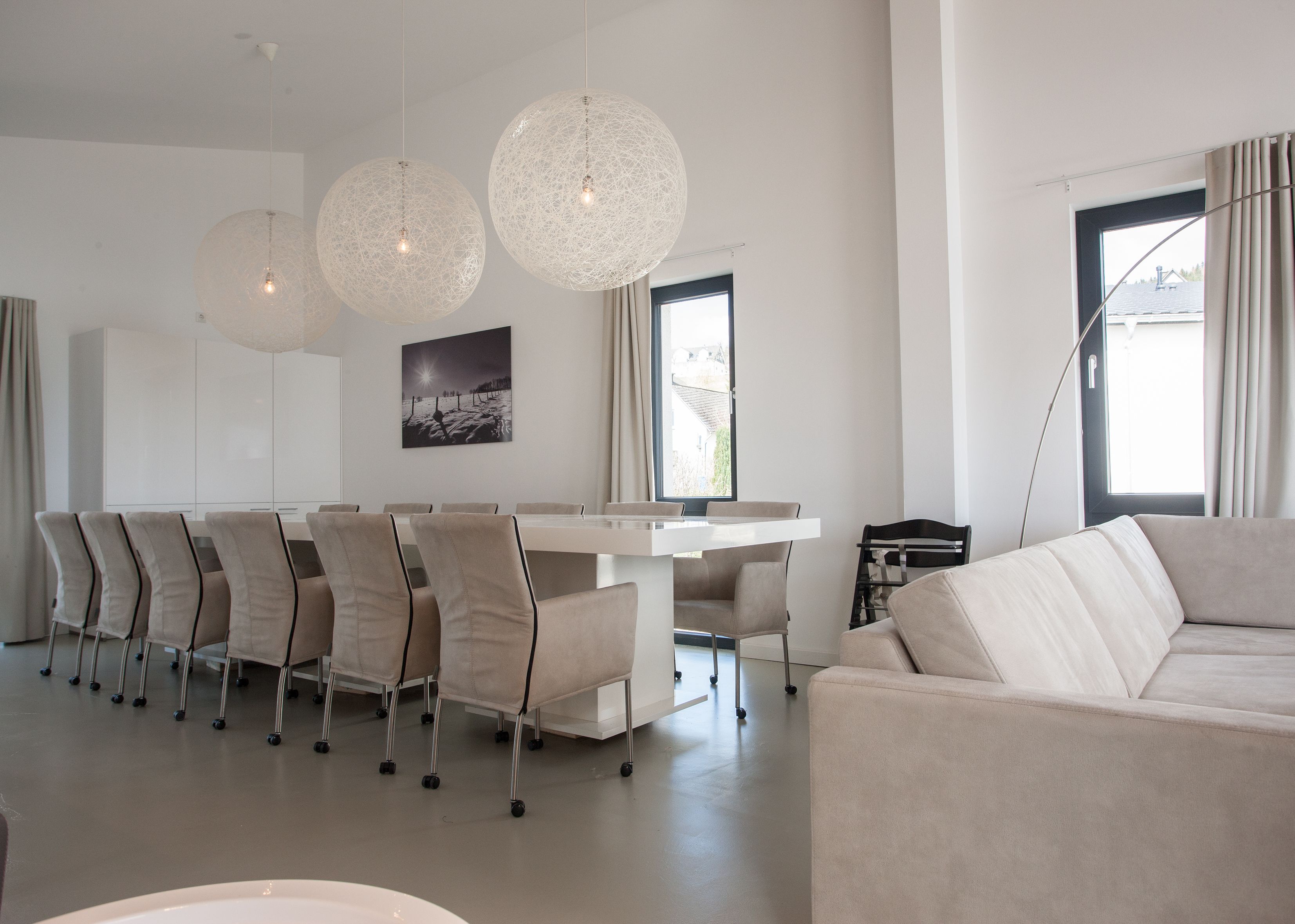 A modern living room with a large sofa, a dining area with a table and chairs, and two spherical hanging lights.