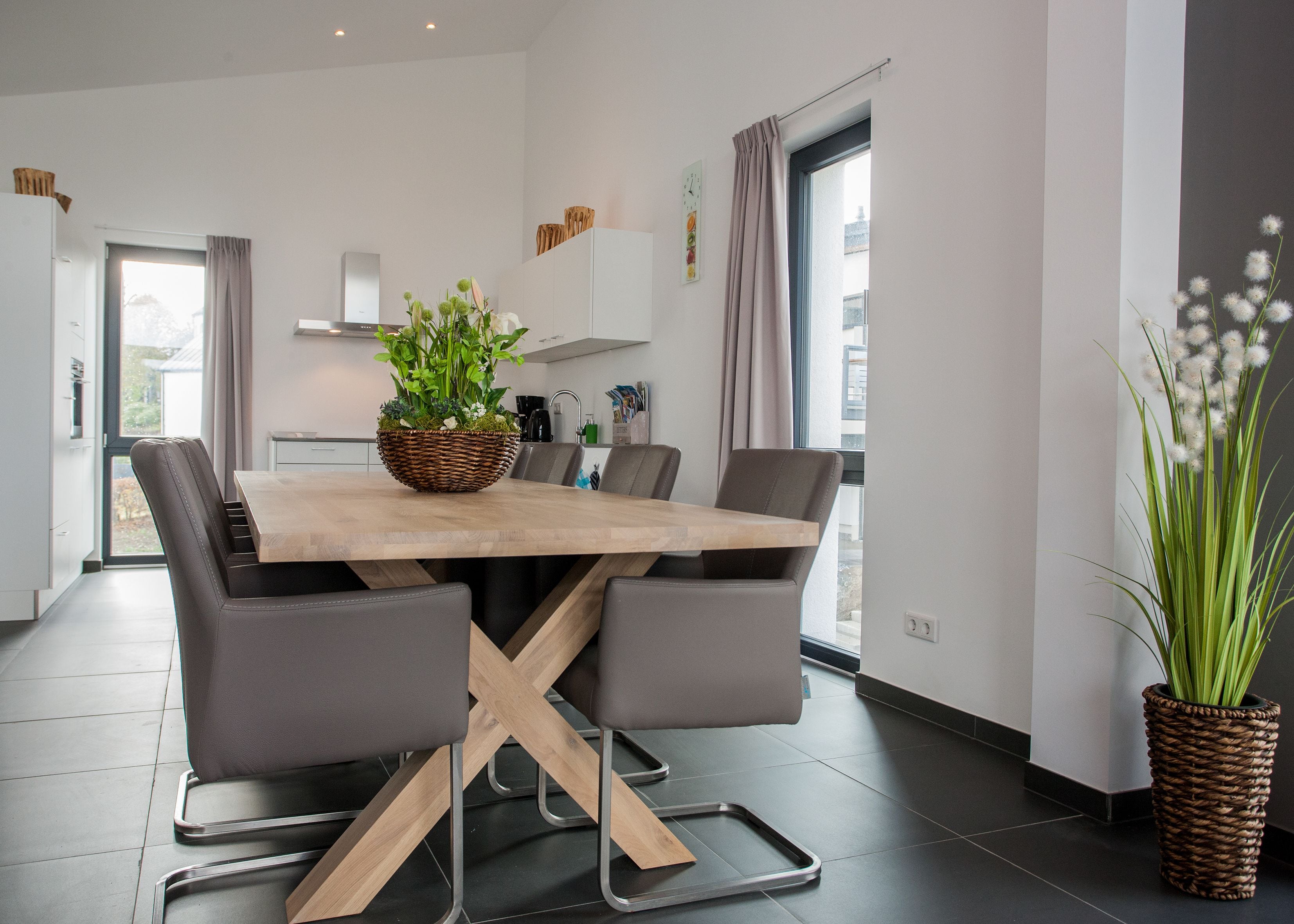 Un espace repas moderne avec une table en bois, des chaises recouvertes d’un tissu gris et un panier tressé contenant des plantes.