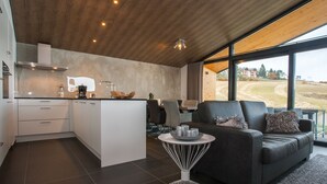 A modern kitchen with a central island, a dining area with a sofa and table, and large windows offering a view of the countryside. - Villas Winterberg (Winterberg)