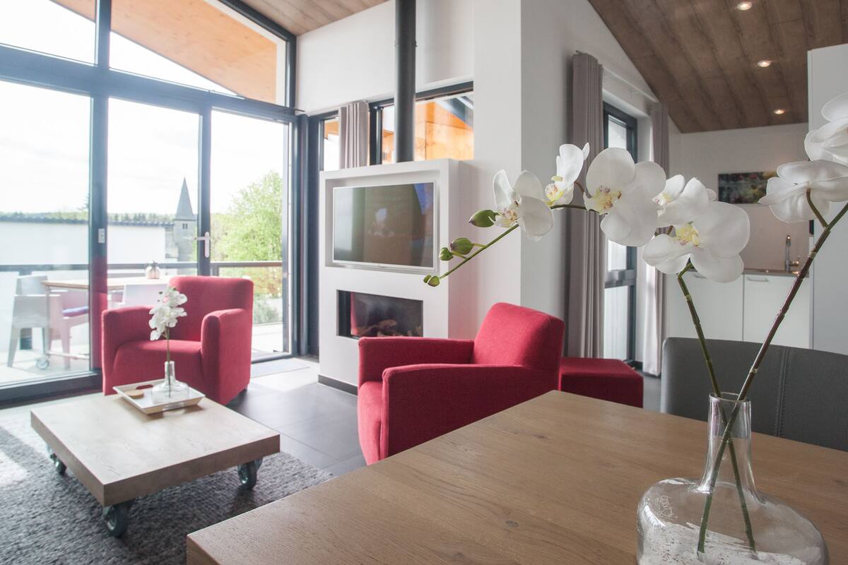 A modern living room with red sofas, a wooden coffee table, and white orchids in a vase.