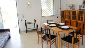 Een eetgedeelte met een houten tafel voor vier personen, omringd door stoelen, een klein wandrek en een raam met een metalen traliewerk.
