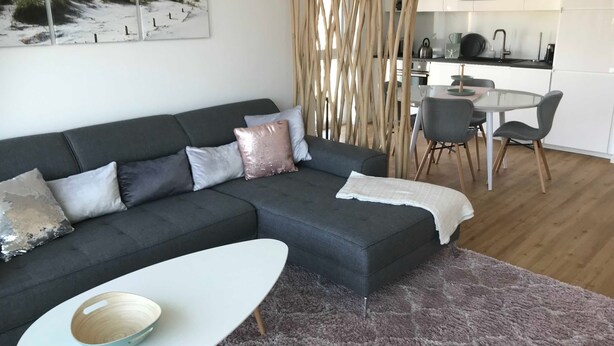 Una sala de estar moderna con un sofá gris, una mesa de centro blanca y un comedor con una mesa y sillas blancas.