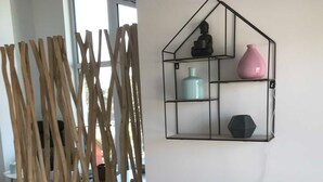 Una habitación con un panel decorativo de madera, un estante fijado a la pared con diversos objetos, y una regleta en una mesa.