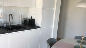 Una cocina moderna con armarios blancos, encimera negra y un pequeño comedor con una mesa y dos sillas.