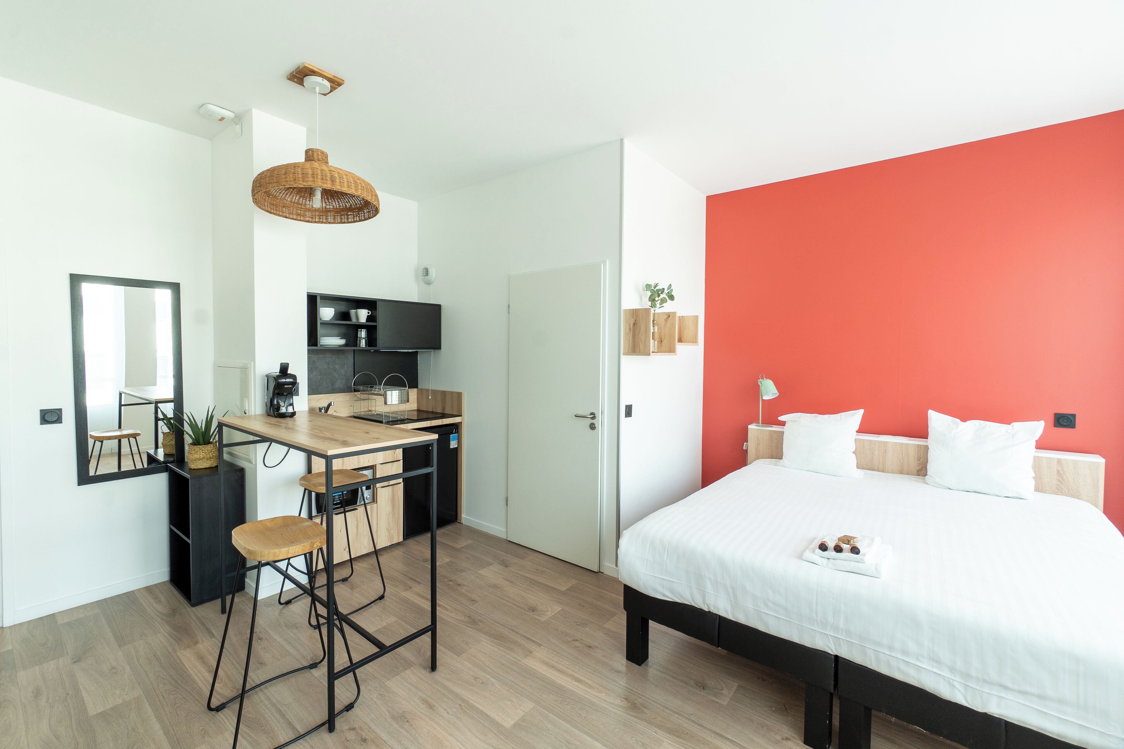Un dormitorio moderno con una cama grande, una pared de acento roja, una kitchenette y un comedor.