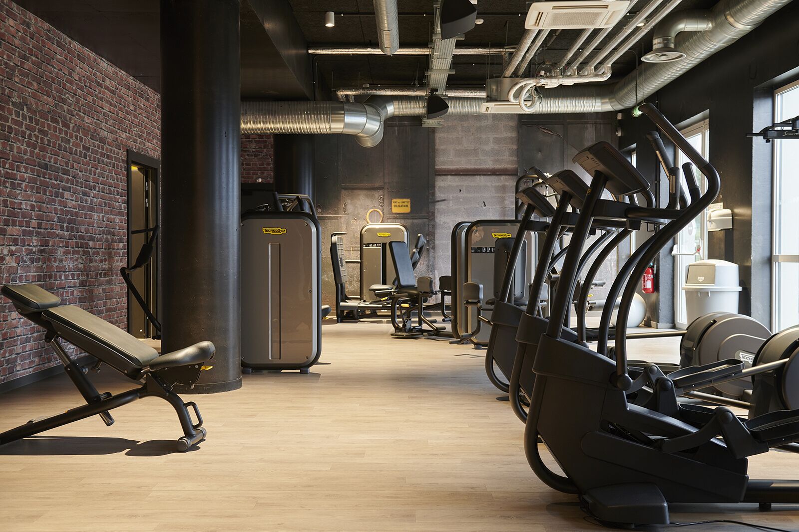 Un gimnasio con equipo de ejercicio, paredes de ladrillo y ventanas grandes.