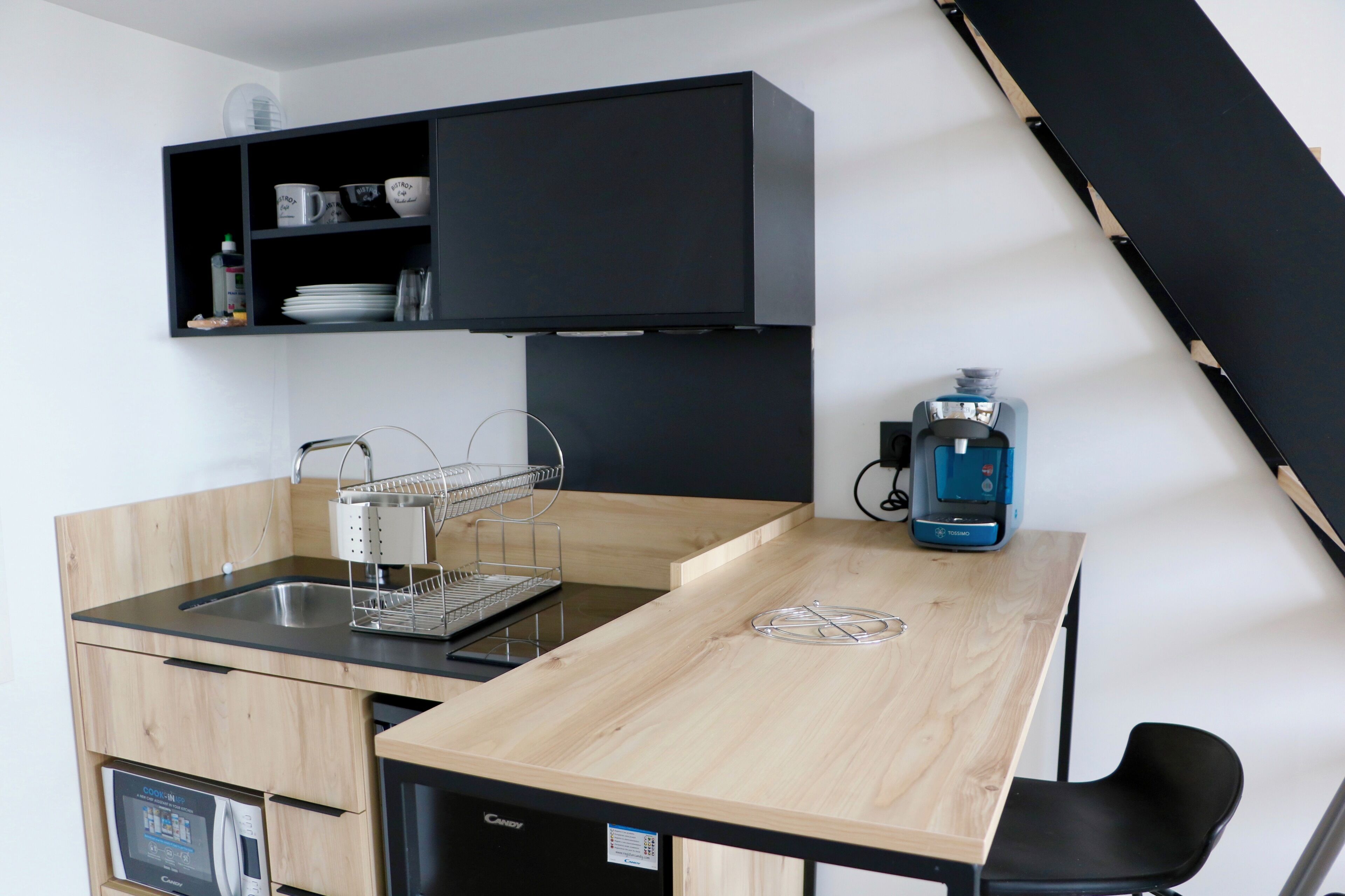 A compact kitchen with a black cabinet, a coffee machine, and a sink.