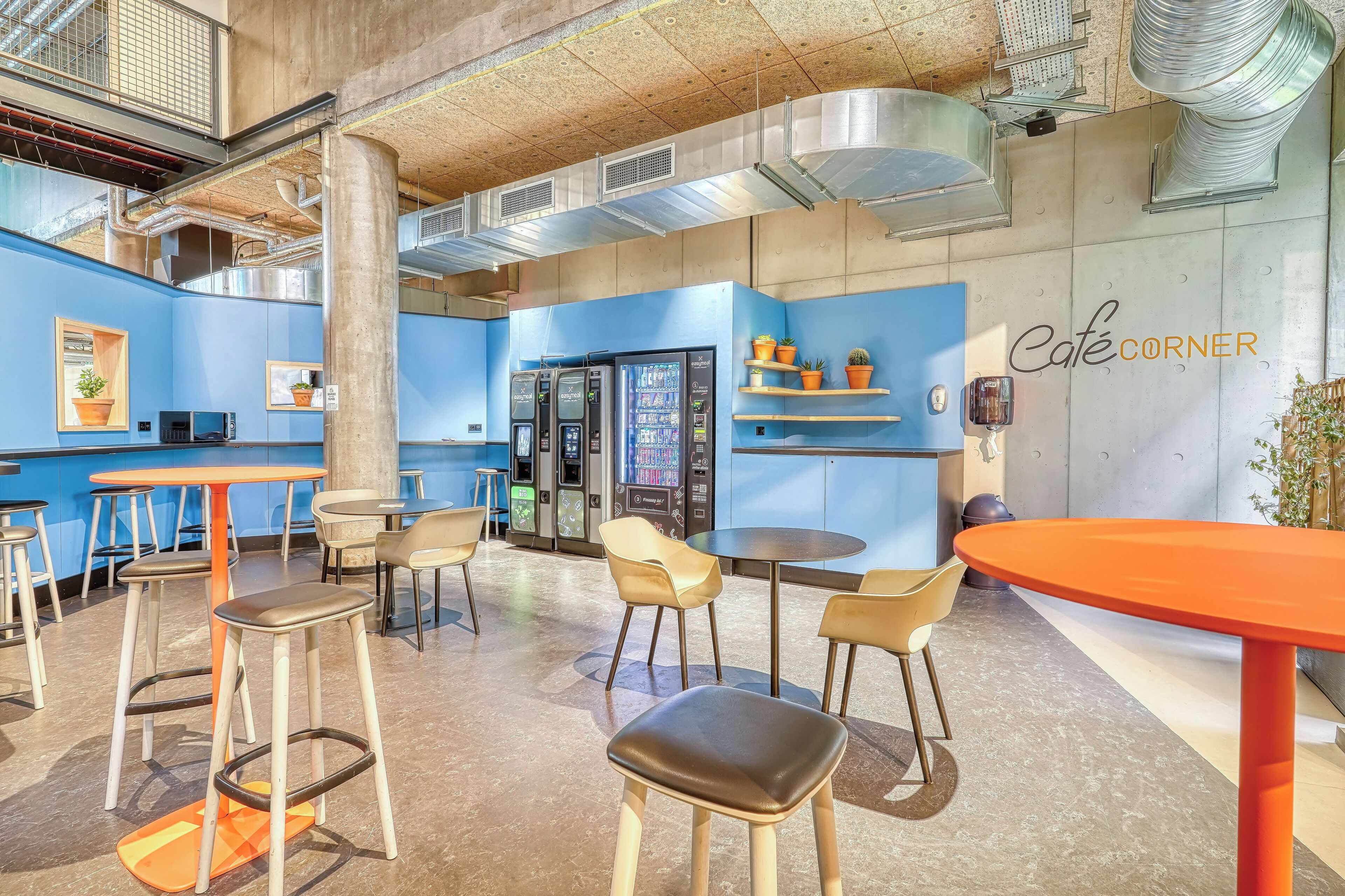 A modern café interior with high ceilings, exposed ductwork, and a blue color scheme.