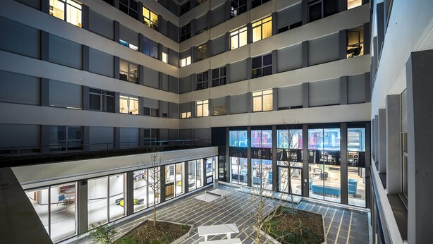 A multi-level atrium with glass walls, outdoor seating, and a central planter area. - Ecla Paris Massy Palaiseau (Palaiseau)