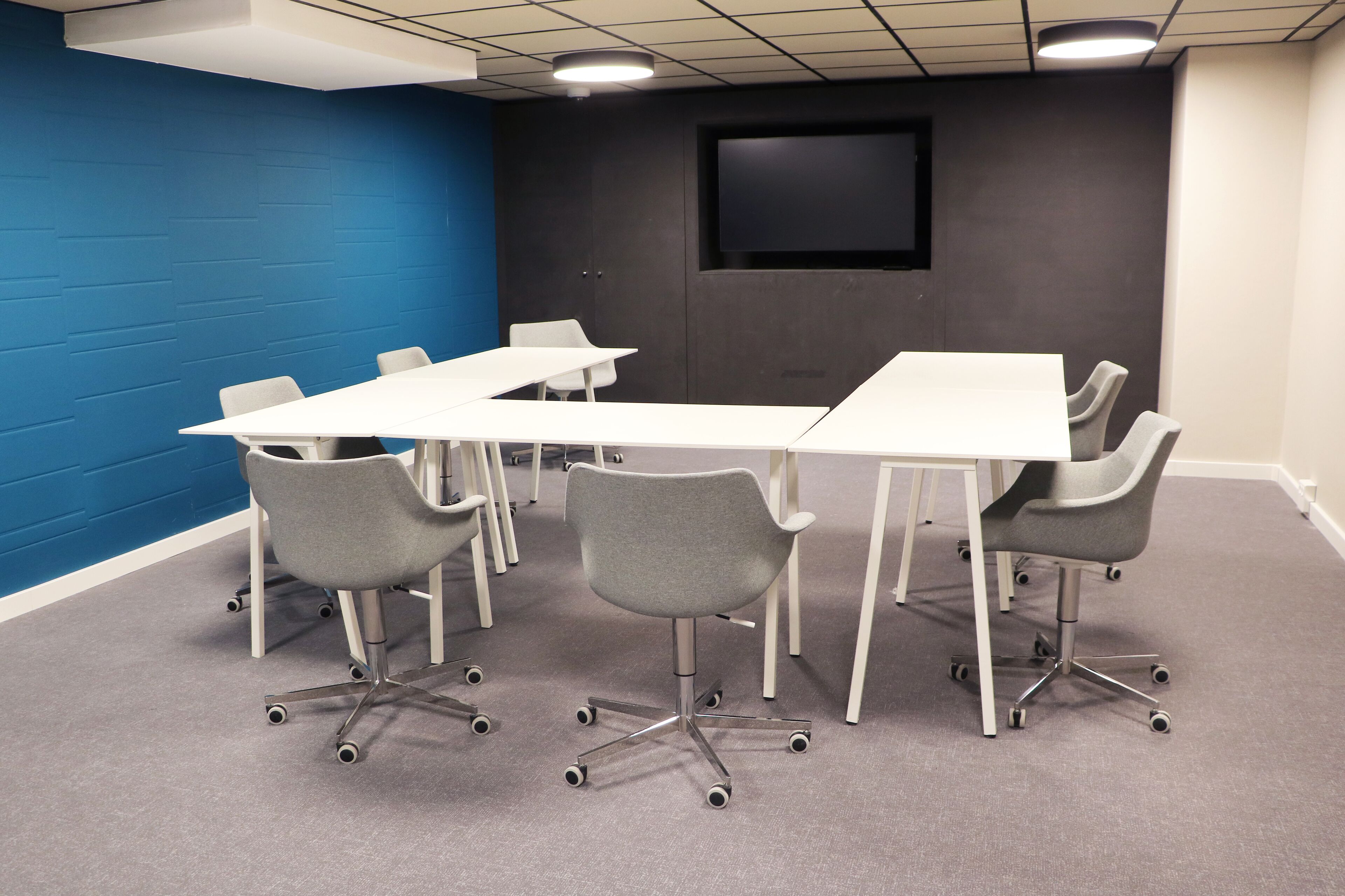 A conference room with a white table, grey chairs, and a blue accent wall.