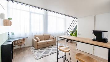 A modern living space with a sofa, a dining table, a kitchen area, and a staircase leading to an outdoor area.