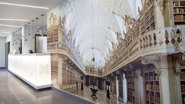 Un lobby imponente con un techo alto, columnas ornamentales y un mural grande que representa una escena clásica.