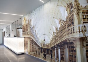 Un lobby imponente con un techo alto, columnas ornamentales y un mural grande que representa una escena clásica.