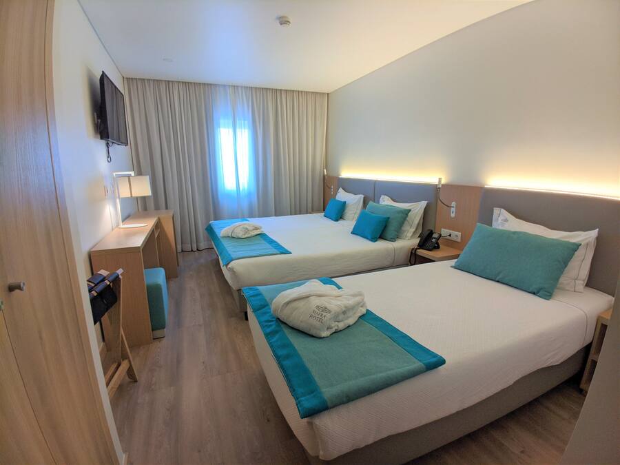 A hotel room with two beds, a desk, a TV, and a window with curtains.