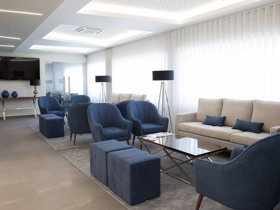 A modern living room with a sofa, armchairs, and ottomans, a coffee table, and a TV mounted on the wall.