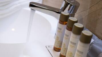 Un baño con un lavamanos blanco, un espejo y cuatro botellas de productos para el cabello sobre el mostrador.