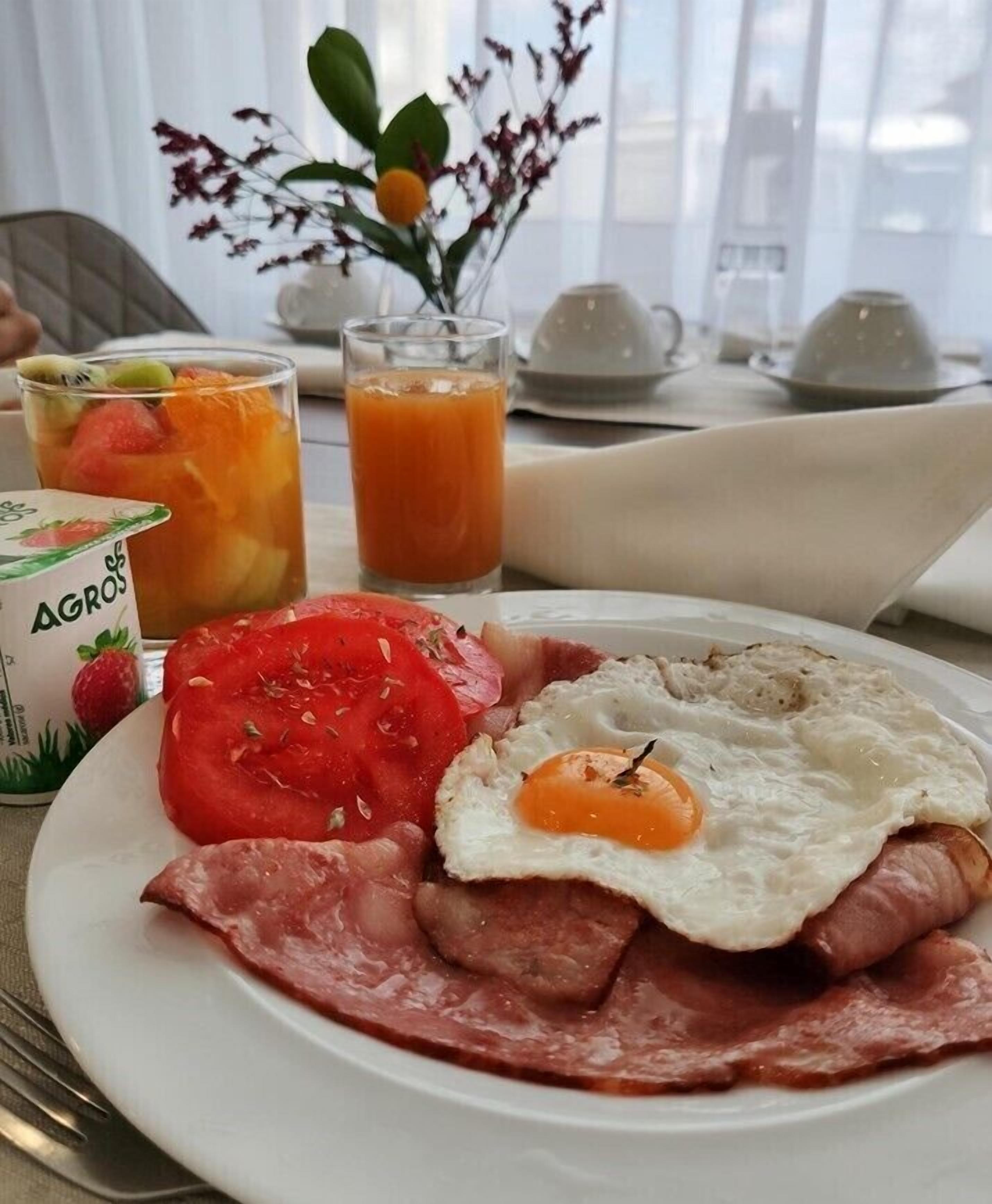 Un plato de desayuno con huevos, tocino, tomate y un vaso de zumo de naranja.