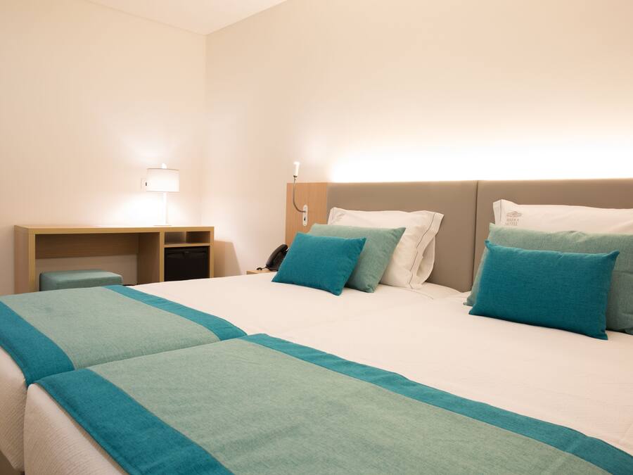 A hotel room with a large bed, two pillows, a desk, and a lamp.