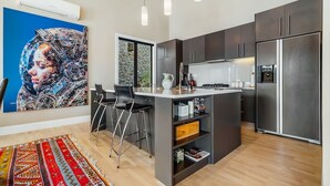 Une cuisine moderne avec des meubles de couleur sombre, un réfrigérateur en acier inoxydable et un îlot central doté de tabourets de bar.