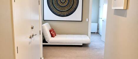 A hallway with a beige carpet, a white sofa with a red pillow, and a large circular artwork on the wall.