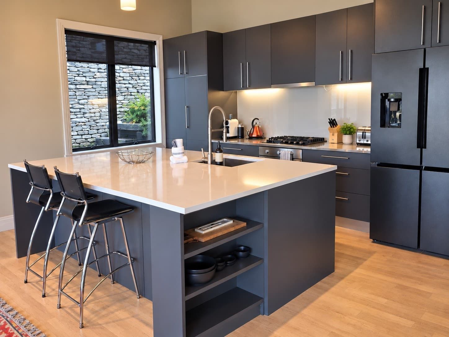 A modern kitchen with a large island, dark cabinetry, and a stone accent wall.