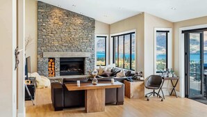 Un salon spacieux doté d’une cheminée en pierre, d’une grande fenêtre offrant une vue panoramique et d’un coin salon moderne.