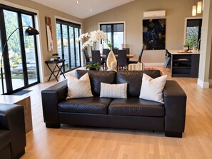 Ein modernes Wohnzimmer mit einer schwarzen Ledersofa, einem Essbereich und großen Fenstern.