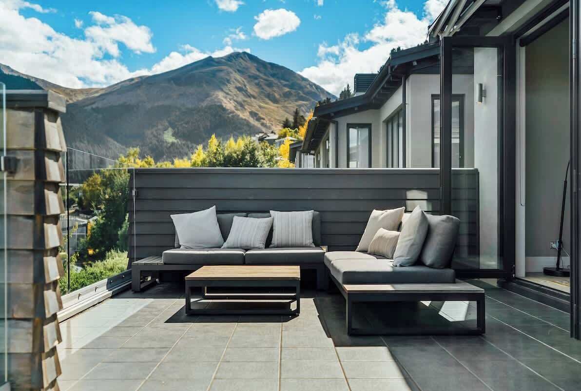 Un espace de vie extérieur moderne, doté d’un canapé et d’une table basse, offrant une vue sur les montagnes et donnant accès, par une porte vitrée, à un patio abrité.