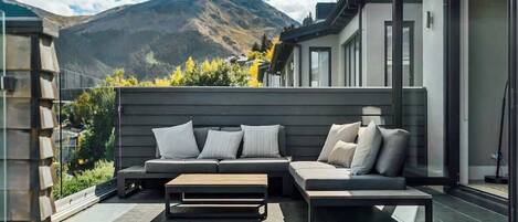 Un espace de vie extérieur moderne, doté d’un canapé et d’une table basse, offrant une vue sur les montagnes et donnant accès, par une porte vitrée, à un patio abrité.