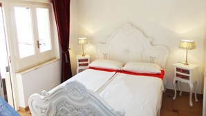 A bedroom with a white ornate bed, two bedside tables with lamps, a red bedspread, and a chandelier. - VersoSud - Casa Torre San Giovanni 17 (Ugento)