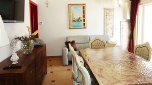 A dining area with a marble table, a chandelier, a painting, and a television on the wall. - VersoSud - Casa Torre San Giovanni 17 (Ugento)