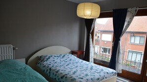 A bedroom with a bed, a nightstand, a window with curtains, and a view of the outside. - Home Trietje Ghent (Ghent)