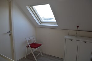Et lille rum med ovenlys, en hvid stol og et skab.
