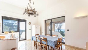 A dining area with a table set for four, wooden chairs, a chandelier, and a view through large windows. - Emma's Villa facing the sea with swimming pool (Racale)