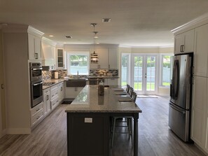 A modern kitchen with white cabinets, a granite countertop, stainless steel appliances, and a large island with bar stools. - Beautiful Large Home Bike to Siesta Key, quiet neighborhood with LOCAL owners!  (Sarasota)